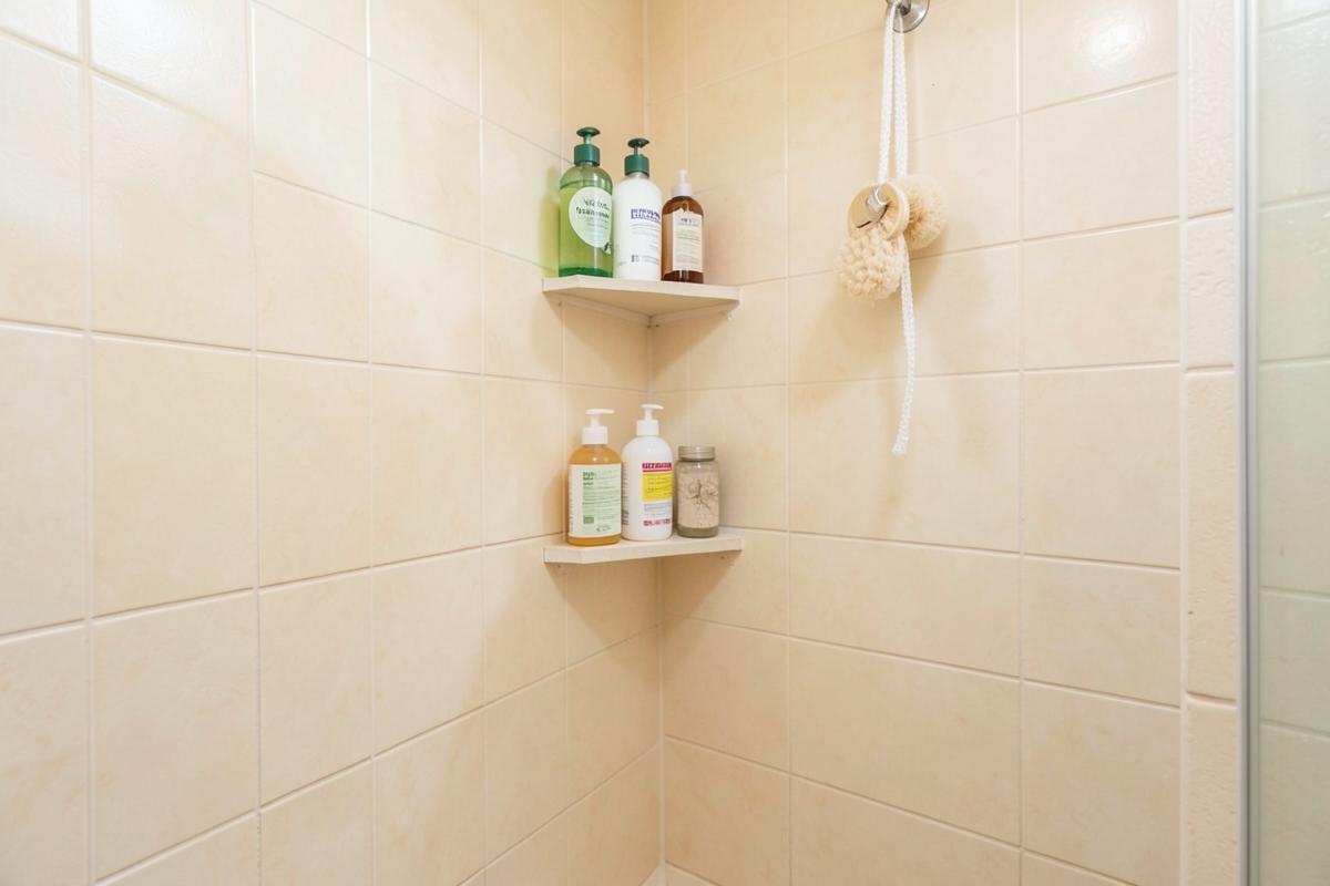 Tidy corner of a small apartment shower with bottles on corner shelves